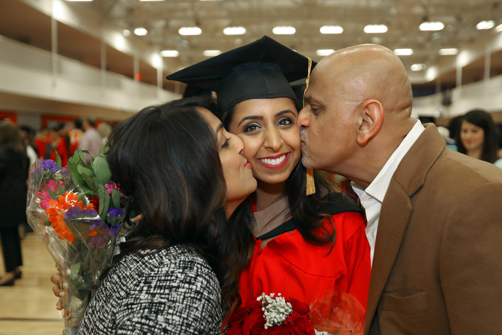A kiss from her parents for a recent graduate in cap and gown.