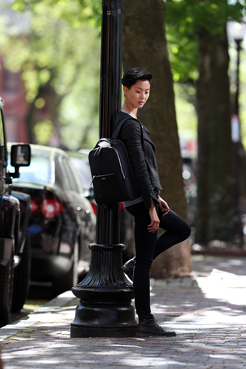 Celebrity chef Kristen Kish is shown with her backpack on a tree lined street.