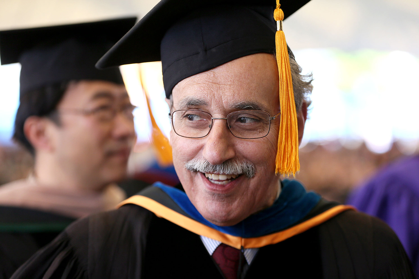 A Suffolk University professor in cap and gown marches into graduation services.
