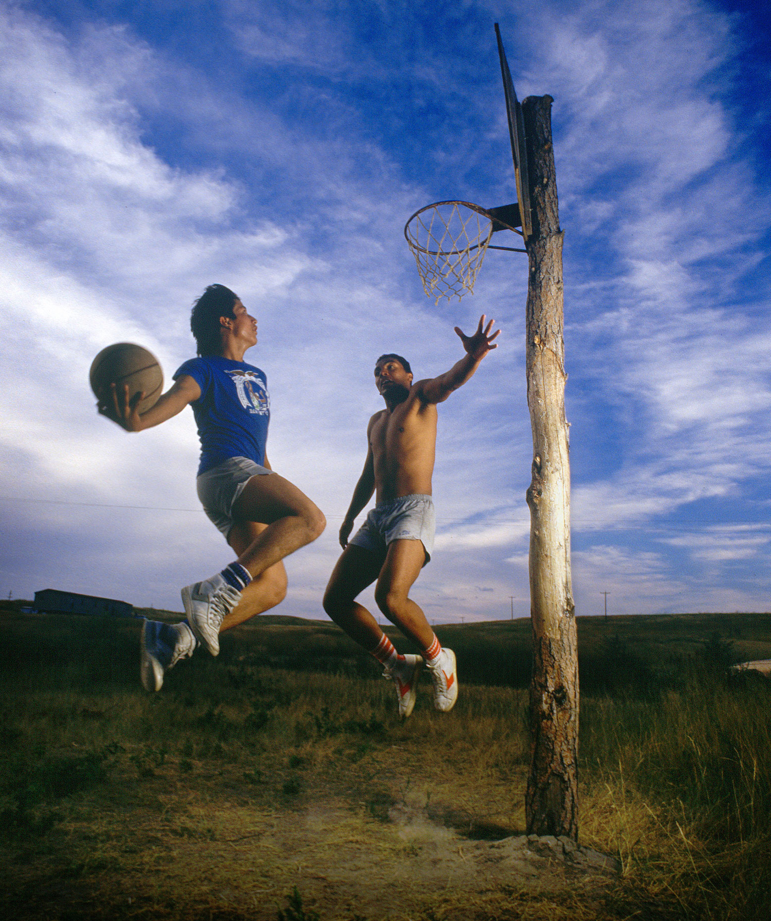 Two native American basketball players use a hoop nailed to a tree to play.