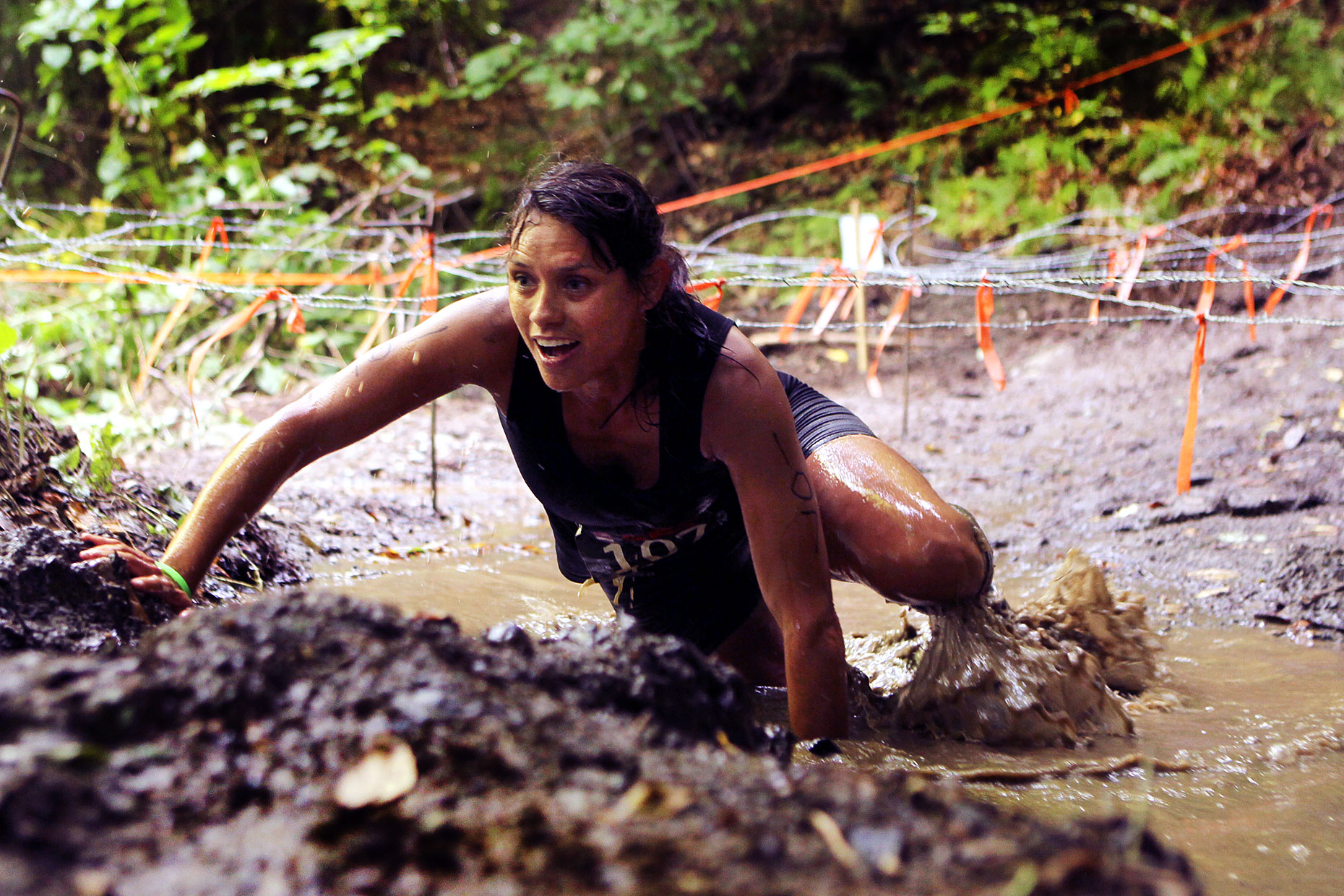 A participant in the Bone Frog challenge competition climbs a muddy slope.